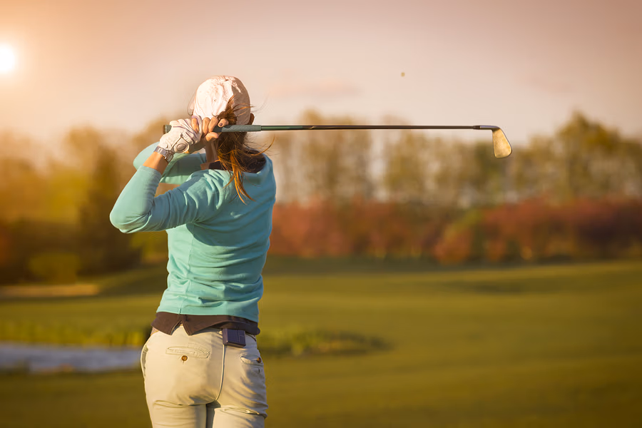 lady hitting a golf ball on a golf course at sunset