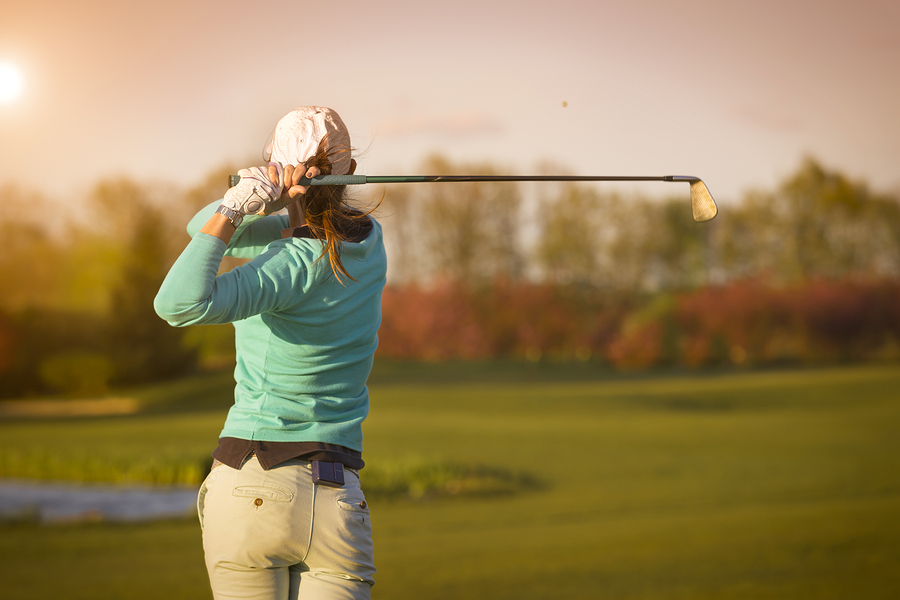 lady hitting a golf ball on a golf course at sunset